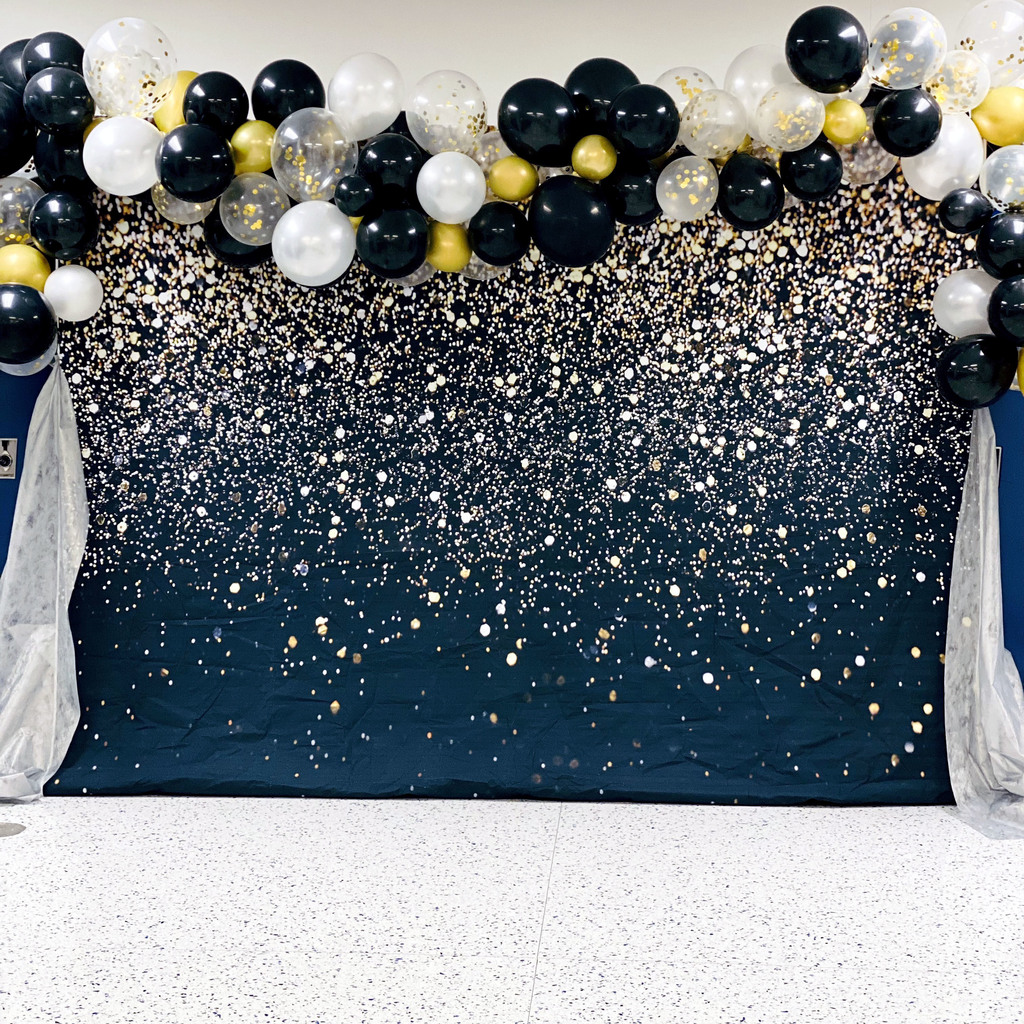 A backdrop for photos: a sparkly background covered in gold glitter and black, white, gold and yellow balloons.