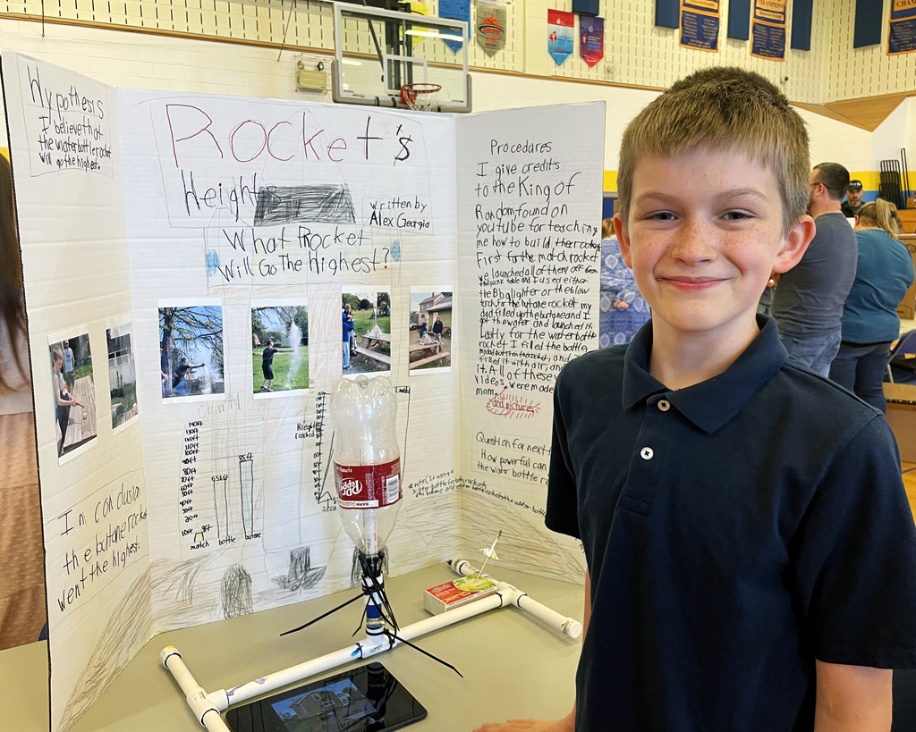 Boy stands in front of an information trifold board on rockets