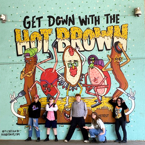 Speech and debate team in front of "Get Down with the Hot Brown" mural